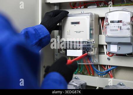 Electrician with screwdriver checking electrical meter indoors, closeup Stock Photo