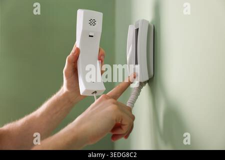 Man with handset pressing button on intercom panel indoors, closeup Stock Photo