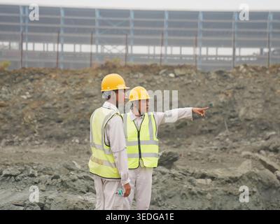 Morowali, Central Sulawesi, Indonesia - January 28, 2026: Two industrial workers wearing safety helmets and reflective vests discussing activities at。 Stock Photo