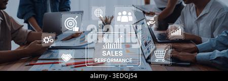 A diverse team collaborates on a sales performance strategy, utilizing laptops and charts while engaging with digital icons showcasing growth and Stock Photo