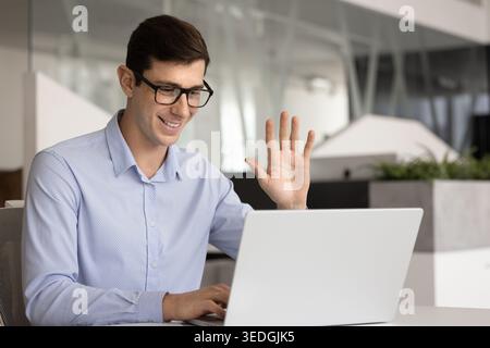 Smiling businessman waving during online meeting at desk Stock Photo