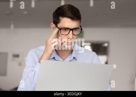 Focused young businessman thinking while working on laptop Stock Photo