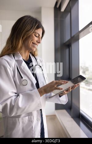 Smiling Hispanic female doctor in uniform working on tablet device Stock Photo