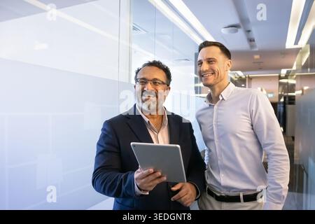 Team members stand in office hallway with digital tablet Stock Photo