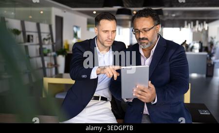 Two focused multiethnic businessmen analyzing information on digital tablet Stock Photo