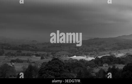 Brooding monochrome view across Wensleydale with layered hills, farms and trees under a dark stormy sky Stock Photo