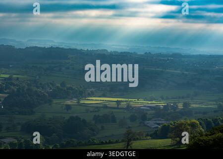 Rays of light breaking through clouds over a misty Wensleydale valley with fields spread below Stock Photo