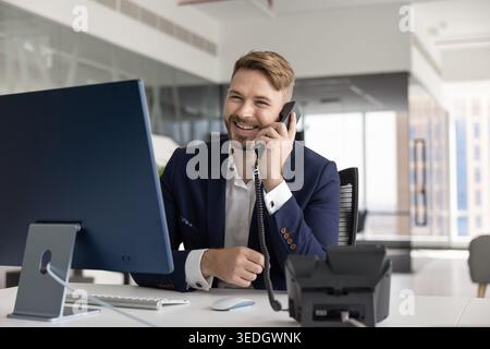 Businessman sits at desk, talking on landline phone Stock Photo