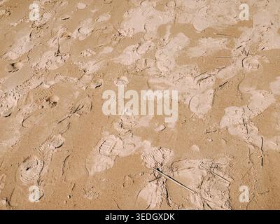 Close-up of footprints scattered across dry sandy beach, creating natural texture and pattern. Ideal background for travel, summer, human presence, or Stock Photo