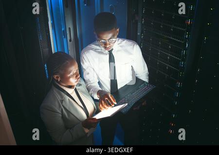 Maintenance, review or team in server room with tech, network or system inspection in data center. Engineers, dark or black people with tablet, fault Stock Photo