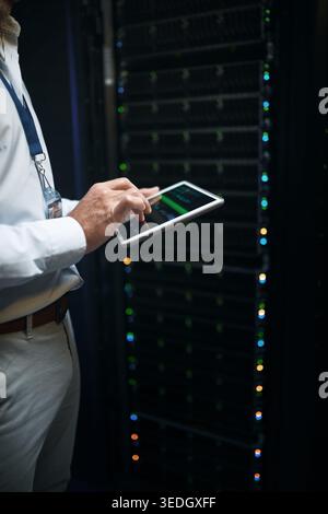 Man, hands and tablet screen with mainframe in server room for cybersecurity maintenance or backup. Person, IT technician or engineer working late Stock Photo