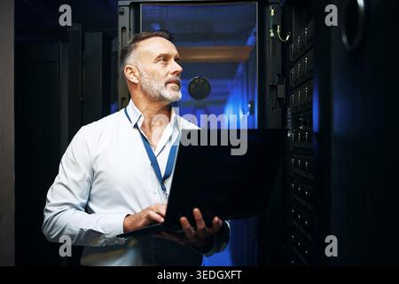 Internet, programmer and man in server room, laptop and cyber security with software development. Mature person, programming and professional in Stock Photo