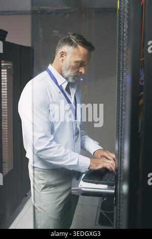 Programming, online and man with laptop in server room, review or troubleshooting for system upgrade. Serious, mature person and network management Stock Photo