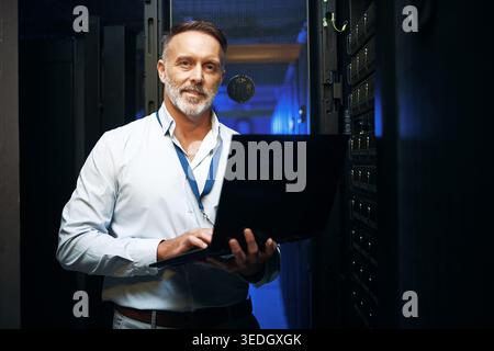 Mature, businessman or portrait with laptop in server room for network security or maintenance. Male person, IT technician or engineer with computer Stock Photo