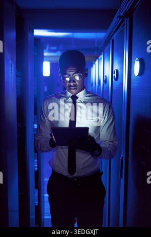 Engineer, man and reading tablet in server room for maintenance, software update or cybersecurity. IT technician, black person and tech in dark data Stock Photo