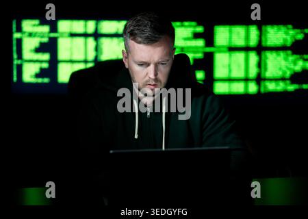Hacker uses computer in dark room. Hacker analyzes system code and data. Hacker monitors secure network connections. Hacker executes cyber crime Stock Photo