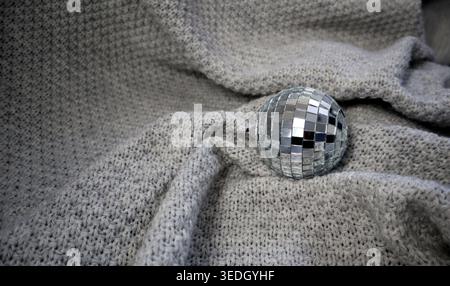 A disco ball sits on a soft gray fabric, reflecting light in a simple indoor space. The texture of the fabric contrasts with the shiny surface of the Stock Photo