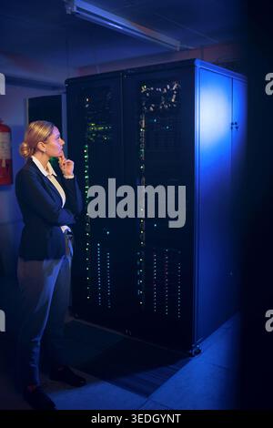 Woman, night and thinking with mainframe in server room for network maintenance or service. Female person, IT technician or system administrator Stock Photo