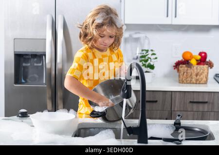 Child playing with foam in kitchen. Cute kid cleaning dishes at home. Happy child splashing soap foam. Funny boy enjoying house chores. Child having Stock Photo