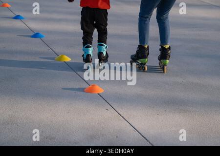 Child and adult roller skating through training cones on paved surface. Concept of learning, coordination, and outdoor sport activity. Suitable for fa Stock Photo