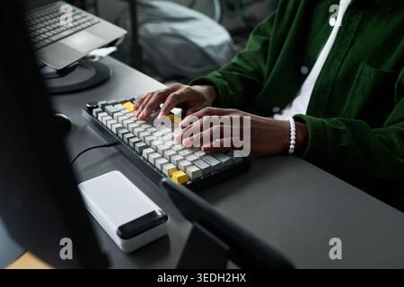 Close up of Black young adult typing on mechanical keyboard at desk, working on computer setup for coding or content production. Ideal for remote work, tech workflow, productivity Stock Photo