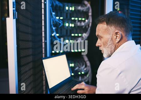 Serious, engineer and man with laptop screen in server room, online or system maintenance on website. Mature person, reading and network management Stock Photo