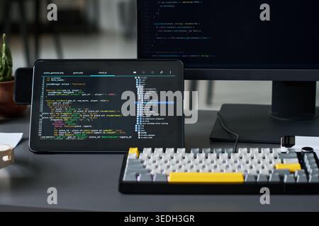 Close up of coding workspace displaying software development on tablet and monitor, showing programming and debugging. Useful for app development, IT training, tech marketing Stock Photo