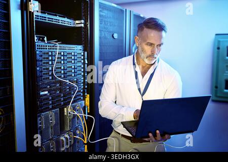 Internet, programmer and man in server room, laptop and problem solving with software development. Mature person, programming and professional in Stock Photo