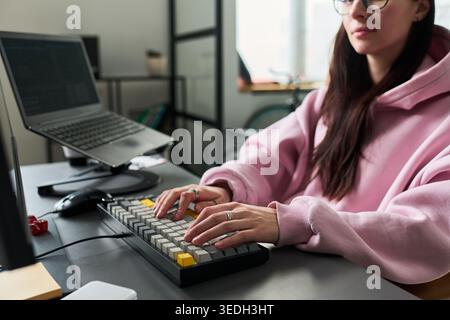 Young adult Caucasian woman typing on keyboard at workstation, working on laptop in home office. Ideal for remote work, coding, productivity, freelance business content Stock Photo