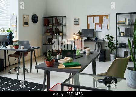Wide angle shot of empty modern office workspace featuring desks, laptops, monitors, and planning board, representing hybrid work setup. Ideal for business productivity, startup Stock Photo