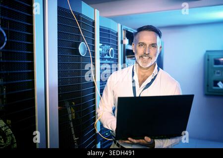 Portrait, programmer and man in server room, laptop and cyber security with software development. Tech upgrade, programming and mature person in Stock Photo