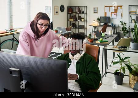 Young Black man and Caucasian woman reviewing desktop screen in office, collaborating on task and solving problem. Useful for teamwork, mentoring, startup workflow marketing Stock Photo