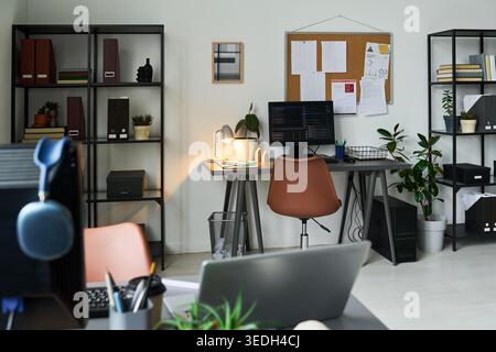 Wide shot of modern office workspace featuring desktop computer, laptop, coding screen, planning board, and organized desks, supporting remote work, startup, or tech business marketing Stock Photo