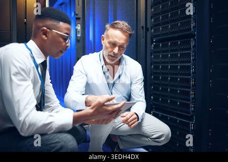 Engineers, tablet or advice in server room for maintenance, programming or security upgrade in business. Men, talking or tech in datacenter for Stock Photo