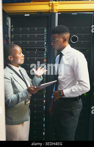 Discussion, manager or engineer with tablet in server room, upgrade or explain mainframe glitch. IT support team, talk or black people in data center Stock Photo