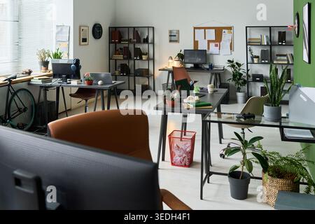 Wide shot of empty modern office workspace featuring desks, computers, shelving, plants, and bicycle. Supporting business workplace, startup branding, recruitment, and productivity themes Stock Photo