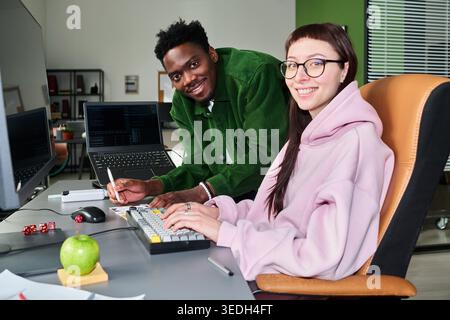 Portrait of Black man and Caucasian young woman coding and collaborating at workstation in office, showing tech teamwork and software development use for IT hiring or startup marketing Stock Photo