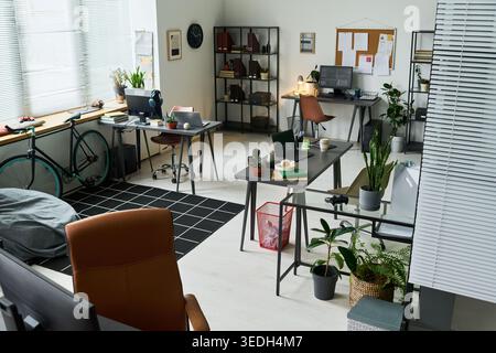 Wide angle shot of modern creative office featuring empty workstations, computers, shared desks, bicycle, plants, supporting startup workspace, hybrid work or coworking marketing Stock Photo