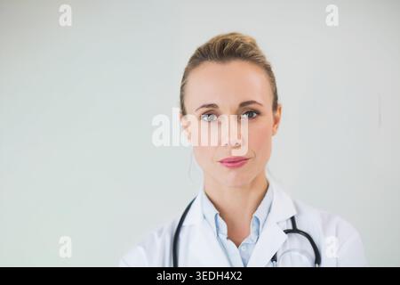 Middle-aged female doctor posing in studio, wearing white lab coat, blue shirt with stethoscope. Clinician, headshot, medical, healthcare, professiona Stock Photo