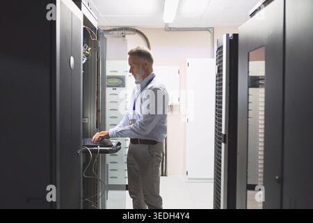 Server room, engineer and typing with laptop for cybersecurity, maintenance or digital storage. Mature person, AI network and machine learning for Stock Photo