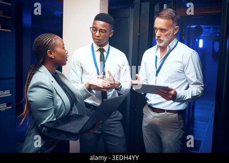 People, tablet and team with maintenance in server room fo cybersecurity, insight or collaboration. Men, woman and technician and laptop with talk Stock Photo