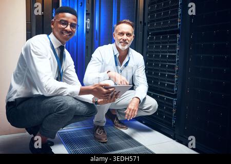 Men, tablet and team with smile in server room with cybersecurity, problem solving or collaboration. Programmer, tech and app with maintenance for Stock Photo