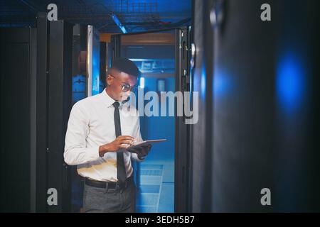 Tablet, technician or black man in data center for software upgrade, inspection or firewall update. Cyber security, tech or person in server room for Stock Photo