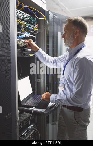 Server room, engineer and connection with laptop for cybersecurity, maintenance or digital storage. Mature person, AI network or machine learning for Stock Photo