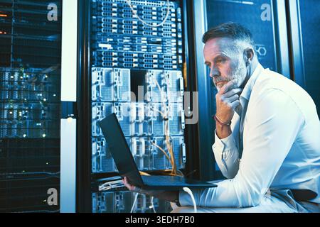 Thinking, engineer and man with laptop in server room, online and troubleshooting for system upgrade. Serious, mature person and programming with Stock Photo