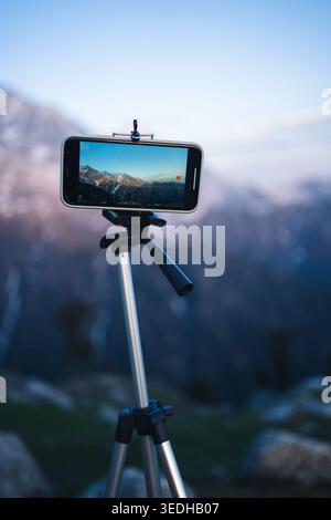 A mobile phone mounted on a tripod capturing a scenic mountain view at dusk in Triund, Mcleodganj, Himachal Pradesh, India. Stock Photo
