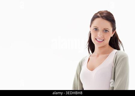 Woman in 20s posing at right of white backdrop, wearing pink camisole and cardigan, copy space. Portrait, headshot, studio, minimal, pastel, casual, h Stock Photo