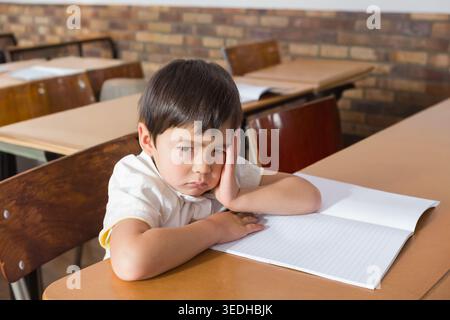 Asian child sitting at school desk, resting head, wearing collared shirt with open lined notebook. Student, classroom, table, papers, quiet, contempla Stock Photo