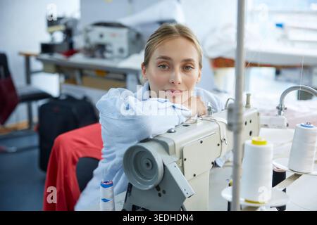 A very creative seamstress is diligently working on her sewing machine in a busy fashion studio Stock Photo