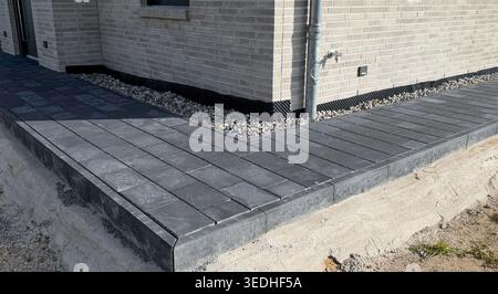 Paved walkway made of gray stone tiles leading to a modern house, featuring a neatly arranged gravel border and a brick wall in the background Stock Photo